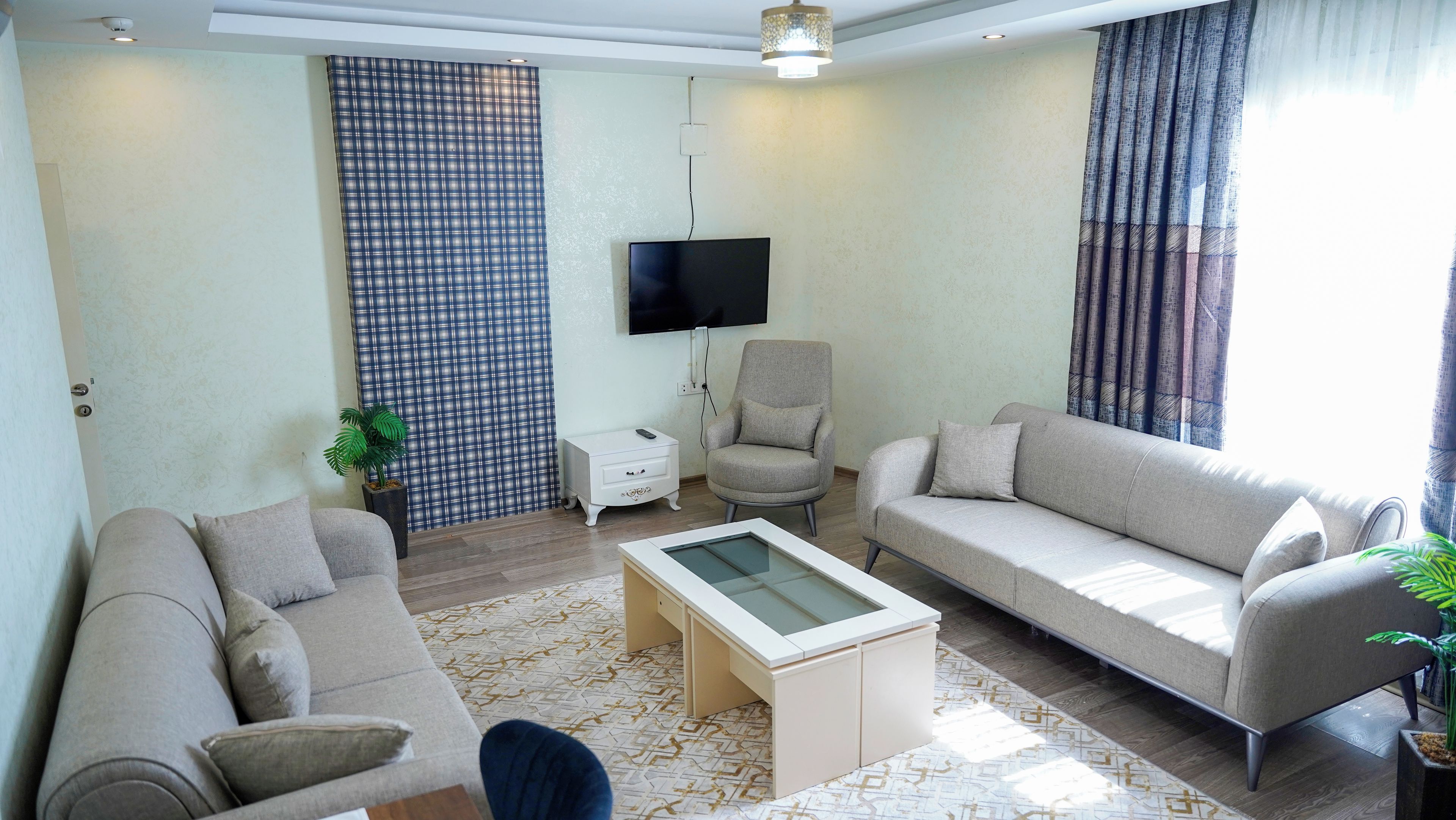 A living room with a sofa, armchair, coffee table, and a TV mounted on the wall.