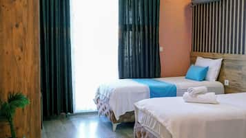 A hotel room with two beds, a wooden wardrobe, a potted plant, and a large window with curtains.