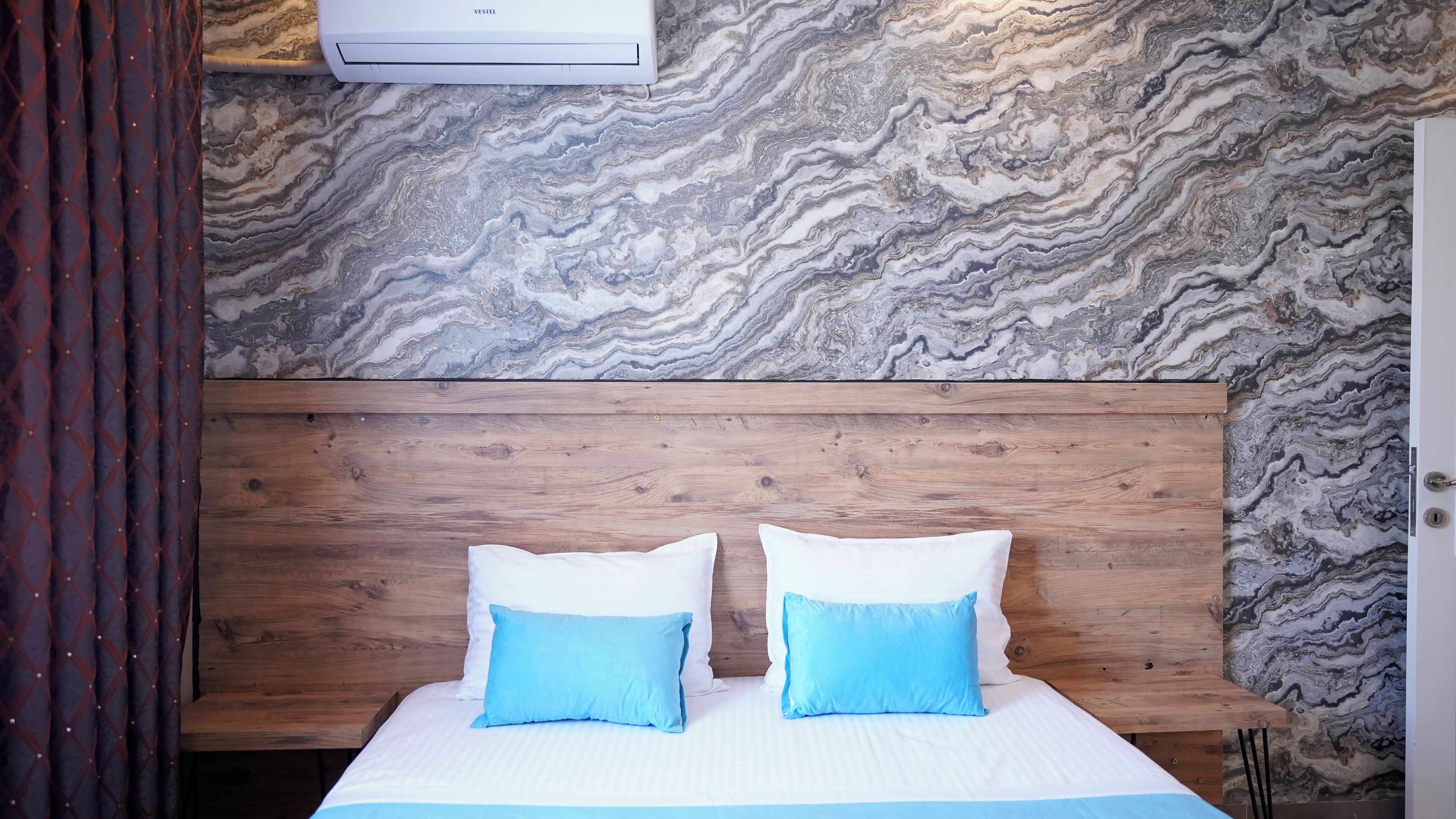 A bedroom with a marble-patterned wall, a wooden headboard, and two pillows.