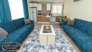 A modern living room with two blue sofas, a coffee table, and a kitchen in the background.