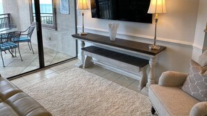 Un salon équipé d’un téléviseur à écran plat, de deux lampes, d’un vase blanc, d’un banc et d’un canapé.