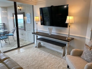 A living room with a flat-screen TV, two lamps, a white vase, a bench, and a sofa.