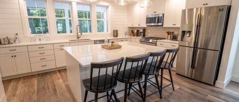 A modern kitchen with white cabinetry, a large island with bar stools, stainless steel appliances, and pendant lighting.