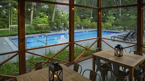 Un espace piscine intérieure avec vue sur une piscine extérieure, des chaises longues et des tables ornées de lanternes.