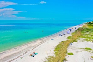 A beach with clear turquoise water, a sandy shore, and people sunbathing.