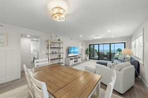 A modern living room with a wooden dining table, white sofas, and a television.