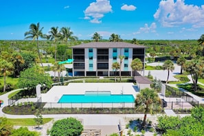 A modern building with a swimming pool, surrounded by palm trees and greenery.