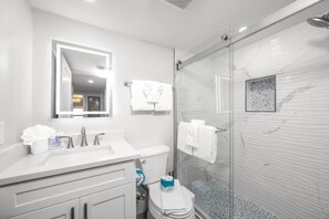 A modern bathroom with a glass shower enclosure, a white sink, and a mirror above the vanity. - Tarpon Beach 206: Beautiful Condo & Stunning Gulf Views to Match (Sanibel)