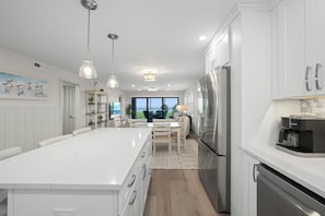 A modern kitchen with white cabinetry, a stainless steel refrigerator, and pendant lighting.