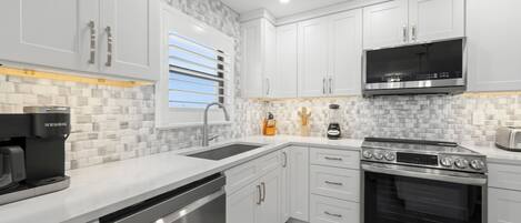 A modern kitchen with white cabinetry, a built-in microwave, a stainless steel dishwasher, and a large oven.