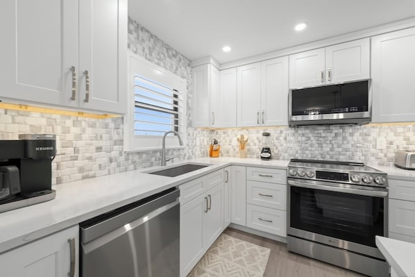 A modern kitchen with white cabinetry, a built-in microwave, a stainless steel dishwasher, and a large oven.