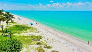 A beach with clear turquoise water, palm trees, and a few people. - Tarpon Beach 206: Beautiful Condo & Stunning Gulf Views to Match (Sanibel)