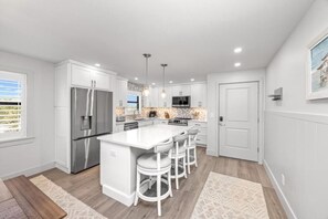 A modern kitchen with white cabinetry, a stainless steel refrigerator, a central island with bar stools, and pendant lighting. - Tarpon Beach 206: Beautiful Condo & Stunning Gulf Views to Match (Sanibel)