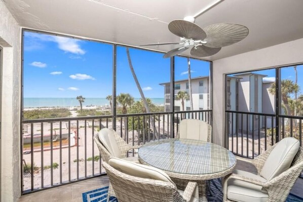 A balcony with a table and chairs, a ceiling fan, and a view of the beach. - Tarpon Beach 206: Beautiful Condo & Stunning Gulf Views to Match (Sanibel)