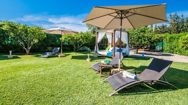 A well-maintained backyard with a wooden canopy bed, two lounge chairs, and a table with a bottle and a bowl. - Central Finca in Mallorca Finca Alegre with pool (Lloseta)