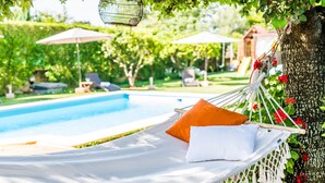 A hammock with white and orange pillows by a pool, surrounded by greenery and a tree. - Central Finca in Mallorca Finca Alegre with pool (Lloseta)