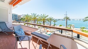 Un balcón con una mesa dispuesta para dos, con vista a un puerto deportivo con barcos y palmeras.
