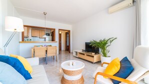 Una sala moderna con sofá, televisor, comedor y cocina visibles a través de una puerta abierta.