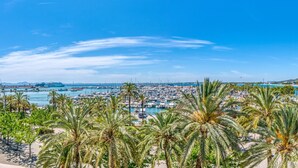 Un paisaje urbano costero con un puerto deportivo, palmeras y montañas al fondo.