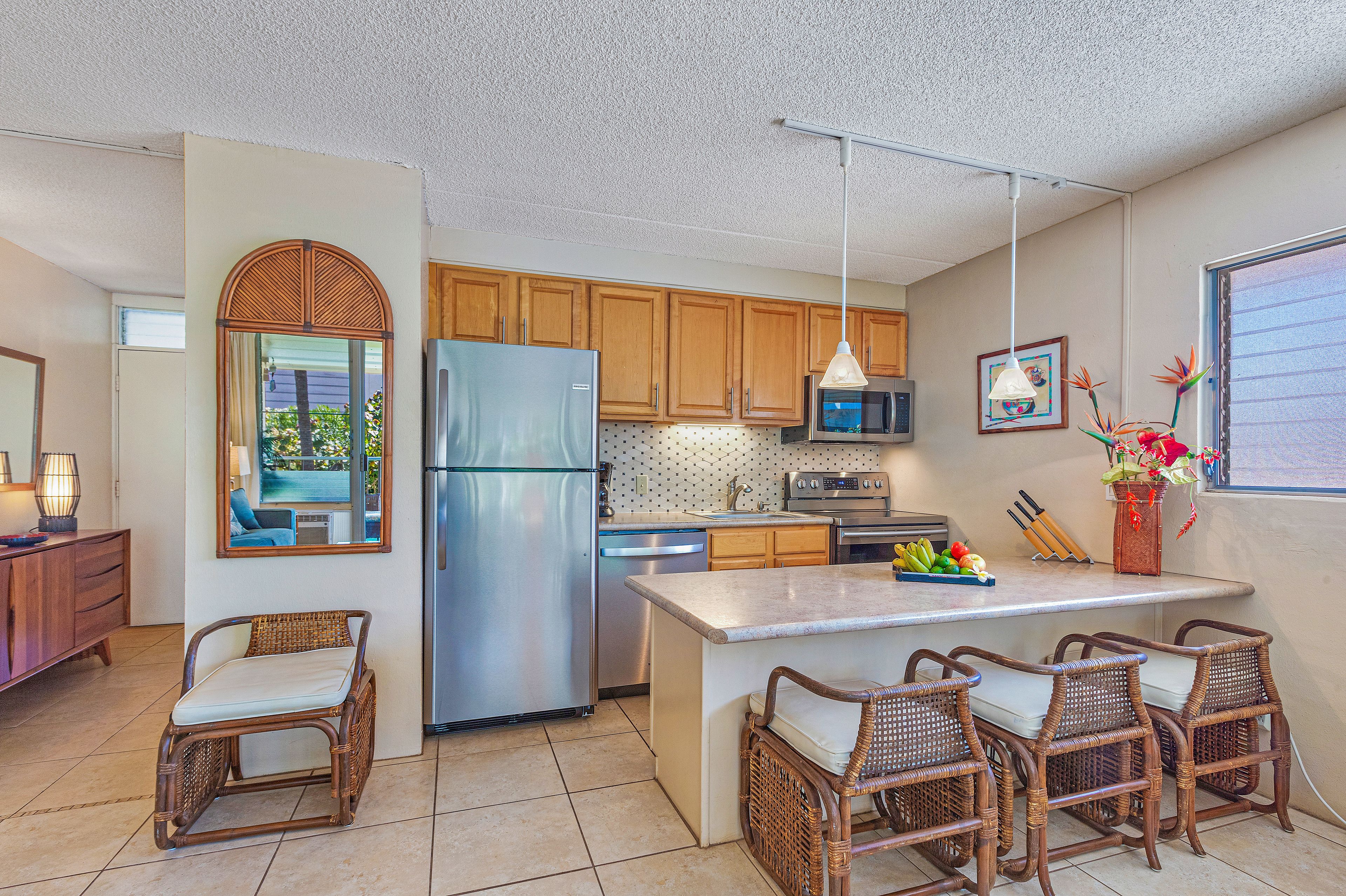 A modern kitchen with wooden cabinets, a stainless steel refrigerator, a microwave, and a dining area with wicker chairs.