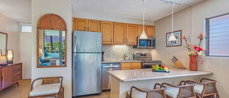 A modern kitchen with wooden cabinets, a stainless steel refrigerator, a microwave, and a dining area with wicker chairs.