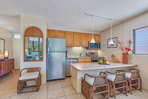A modern kitchen with wooden cabinets, a stainless steel refrigerator, a microwave, and a dining area with wicker chairs.