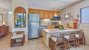 A modern kitchen with wooden cabinets, a stainless steel refrigerator, a microwave, and a dining area with wicker chairs.