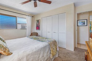 A bedroom with a bed, a ceiling fan, a window with blinds, a radiator, a closet, and a chair.