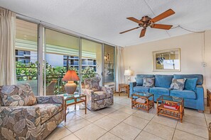 A spacious living room with a blue sofa, patterned armchairs, and a ceiling fan.