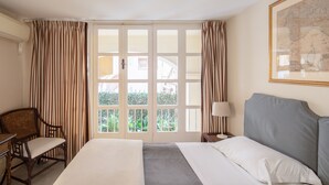 Habitació d'hotel amb un llit, una cadira, un escriptori, una làmpada i una finestra amb cortines.