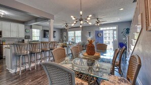 A spacious dining area with a glass table and wicker chairs, a ceiling fan, and a pineapple centerpiece.
