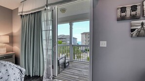 A bedroom with a large sliding glass door leading to a balcony with a view of buildings and a beach.