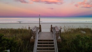 A wooden boardwalk leading to a beach with a clear sky and a sunset.