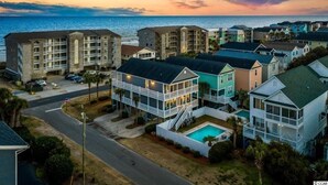 A coastal hotel with multiple buildings, a swimming pool, and a view of the ocean at sunset.