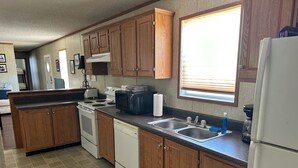 A compact kitchen with wooden cabinets, a stove, a microwave, a sink, and a window with blinds. - KINGFISH LODGE - PRIVATE MAINTAINED 3 BEDROOM 2 BATHROOM PRIVATE RENTAL (Buras)