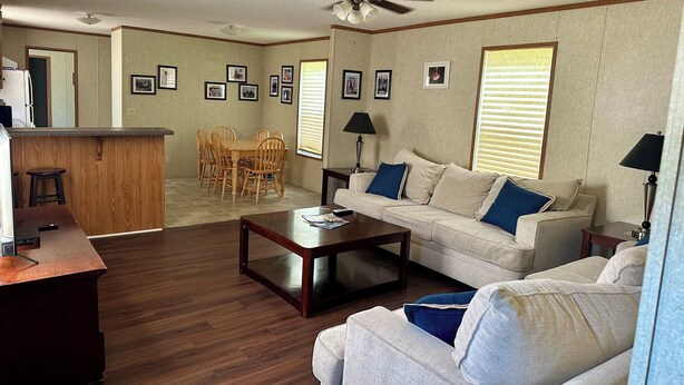 A living room with a sofa, coffee table, and dining area with chairs. There is a ceiling fan and a window with blinds. - KINGFISH LODGE - PRIVATE MAINTAINED 3 BEDROOM 2 BATHROOM PRIVATE RENTAL (Buras)