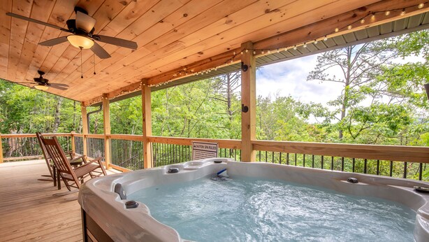 Eine Holzterrasse mit Whirlpool, Stühlen und Deckenventilator.