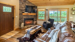 Ein gemütliches Wohnzimmer mit Kamin aus Stein, einer Ledersofa und einer Holzbalkendecke.