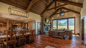 A spacious living area with a stone fireplace, wooden dining table, and a large window offering a mountain view.