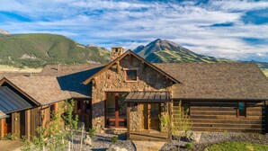 A rustic cabin with a stone facade, wooden exterior, and a view of a mountain range.