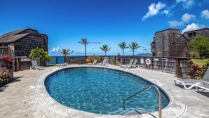 A pool area with clear blue water, surrounded by lounge chairs and a view of the ocean.