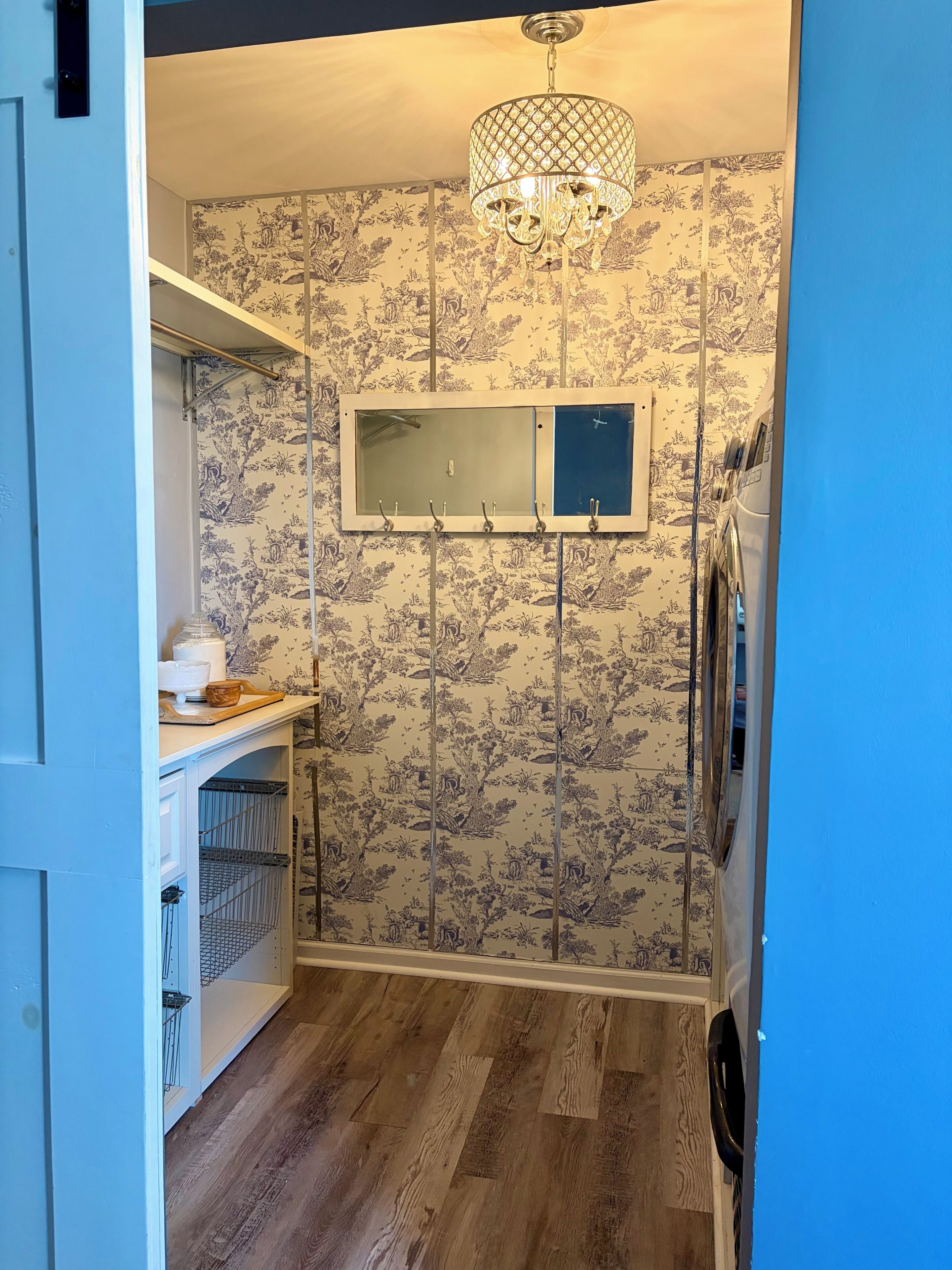 Una cocina compacta con suelo de madera, una lámpara colgante y un espejo decorativo.