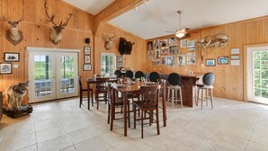 A wooden-paneled dining room with a large table and chairs, a bar area, and various mounted animal heads on the walls.