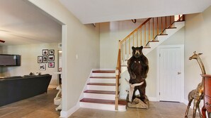A living room with a staircase, a mounted bear, and a giraffe statue.