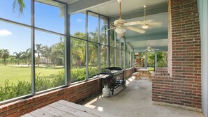 A covered patio with a barbecue setup, large windows, and a brick wall.