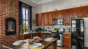 Une cuisine avec des meubles de rangement en bois, un mur en briques, un four encastré, un four à micro-ondes, un réfrigérateur et une table à manger pour quatre personnes.