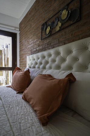 A bedroom with a brick wall, a tufted headboard, and a decorative wall piece. - Unmissable premium loft in a strategic location in la recolETA (Ciudad Autónoma de Buenos Aires, Recoleta)