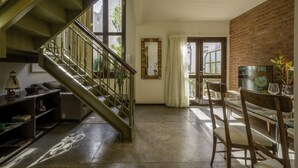 Un escalier menant à un deuxième étage, un coin repas avec une table et des chaises, un miroir au mur et un mur en briques.