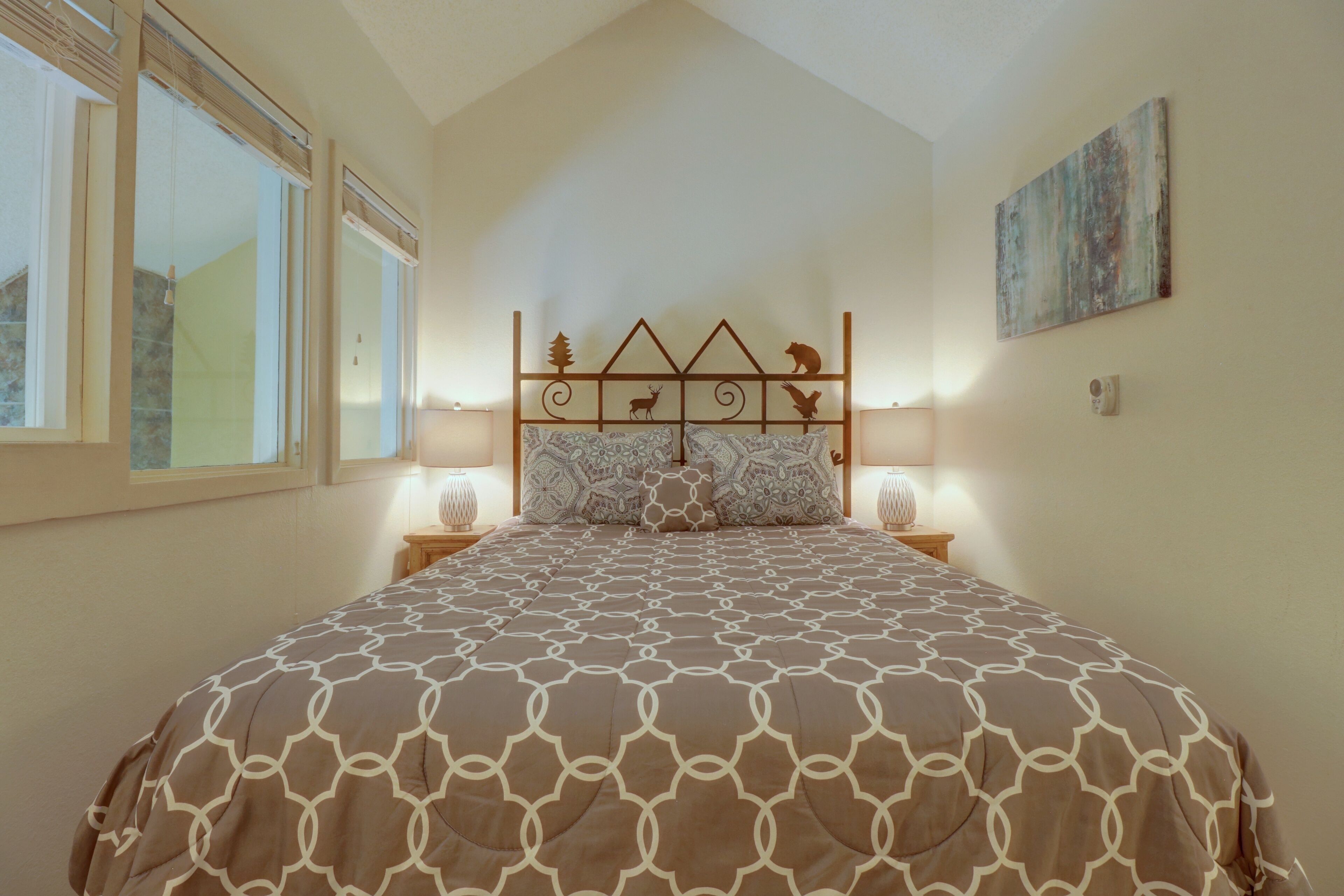 A bedroom with a large bed, a headboard with animal designs, two bedside lamps, and a painting on the wall.