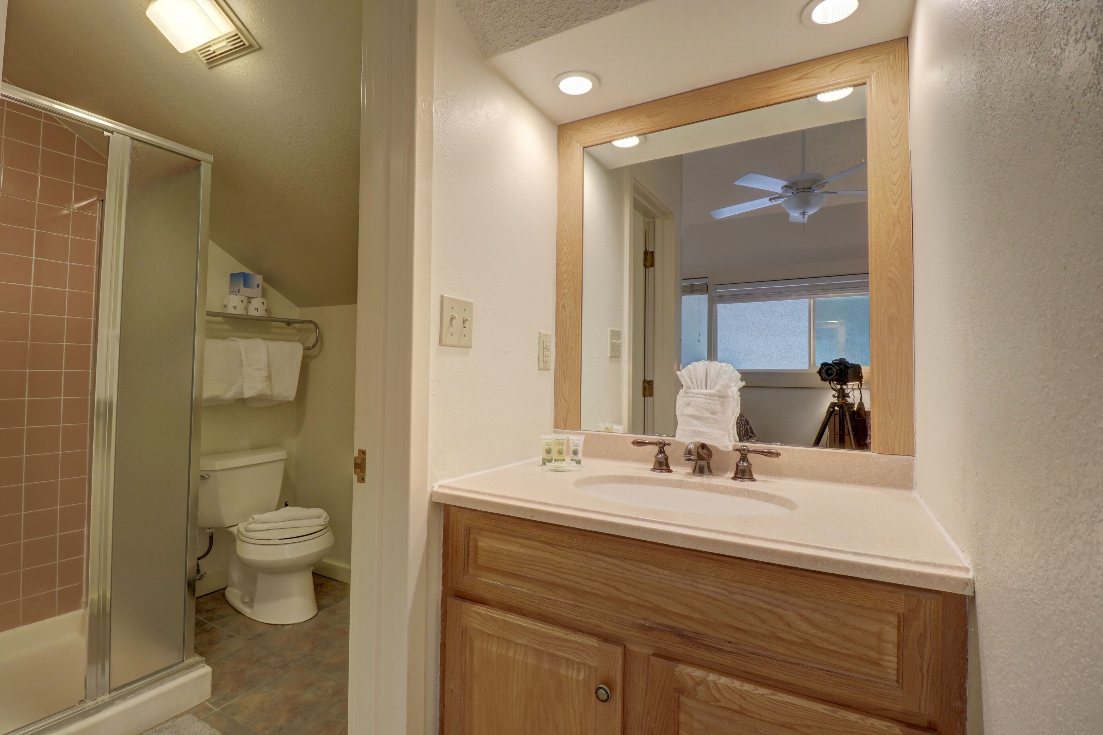 A bathroom with a shower, toilet, vanity, and a ceiling fan.